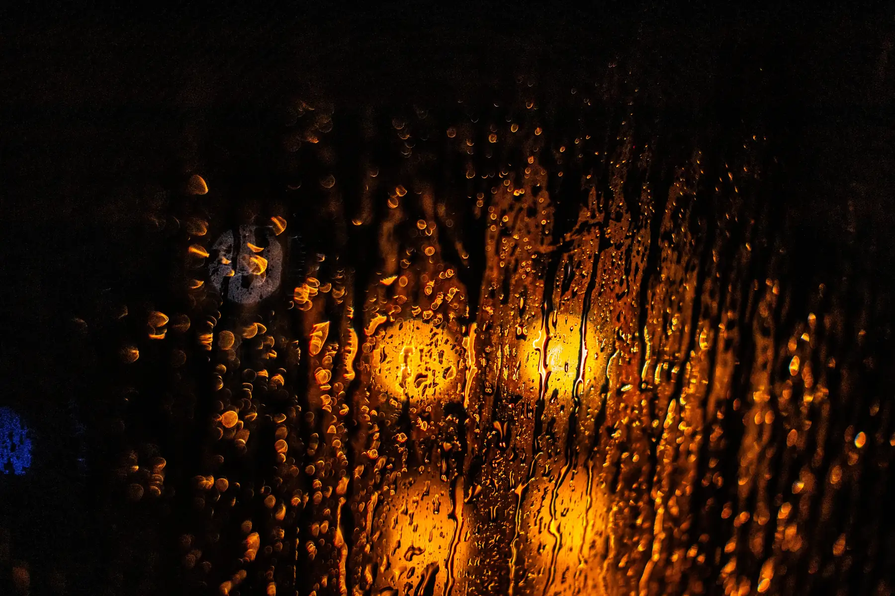 Warmes Licht hinter einer regennassen Scheibe am Abend.