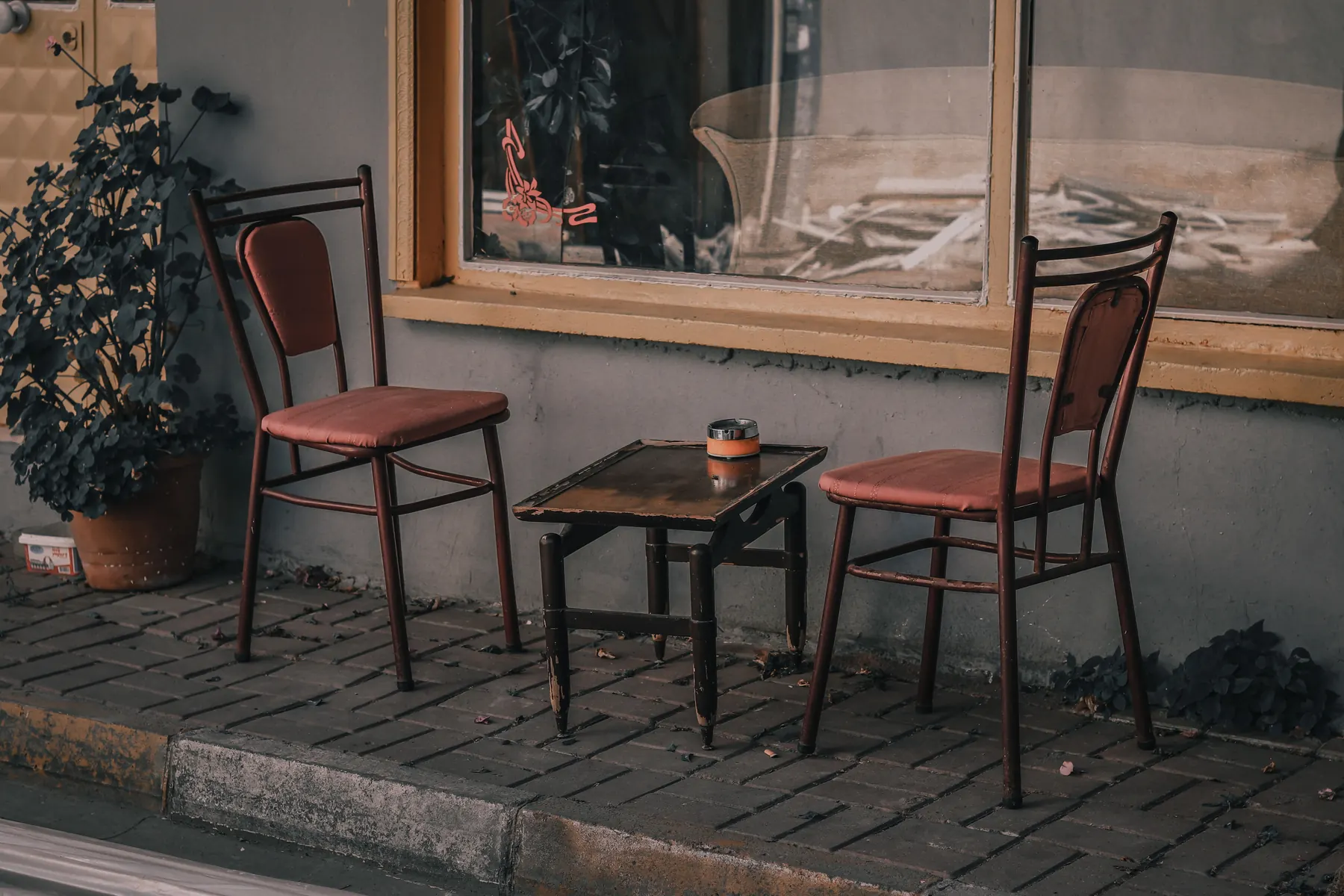 Zwei Stühle und ein kleiner Tisch vor einem Café, ohne Gäste.